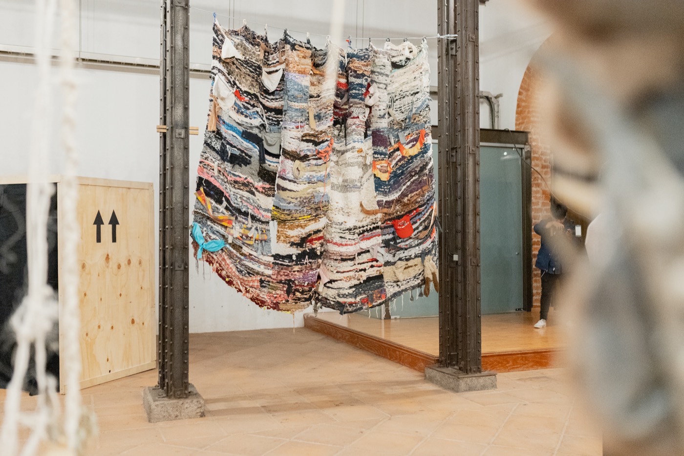 Pieza textil hecha de ropa y telas apiladas, suspendida entre dos columnas de hierro en la sala de Bordear, una idea de frontera. Palacio de la Autonomía, UNAM, 2025.