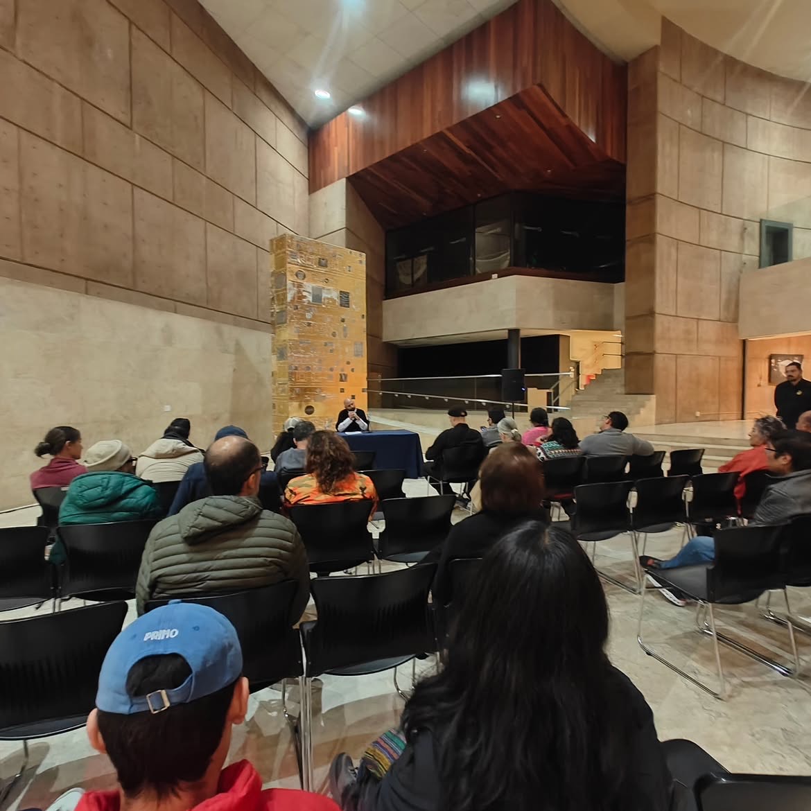 Público sentado en el vestíbulo del Centro Cultural Tijuana, de espaldas, atendiendo la conferencia bajo el volumen de madera del auditorio. Una casa irreconciliada, CECUT, 2025.