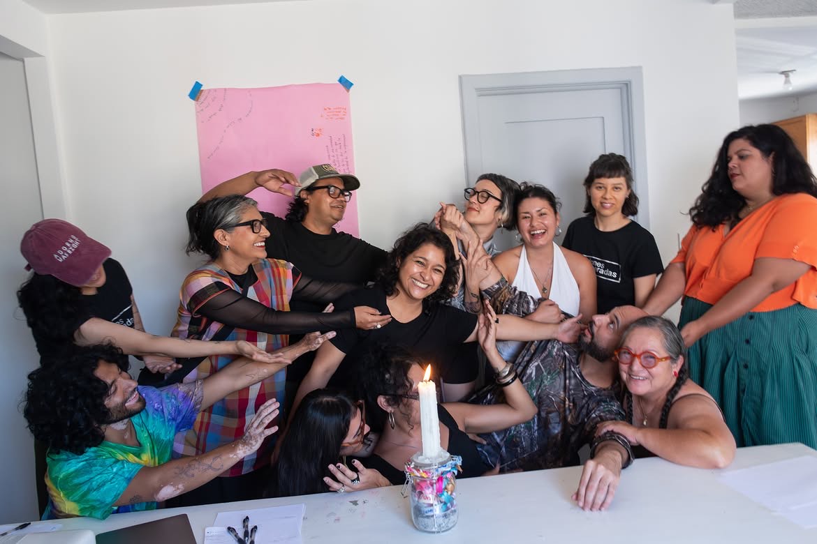 Retrato de grupo del taller: las participantes rodean a una de ellas alrededor de la mesa con la vela encendida al cierre del módulo. Temporada de incendios, Relaciones Inesperadas, Tijuana, 2026.